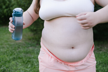 Obese young woman holds her belly. Outdoor exercises