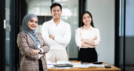 Portrait of young  woman wearing traditional hijab clothes standing in the office with her colleague. Smiling to camera