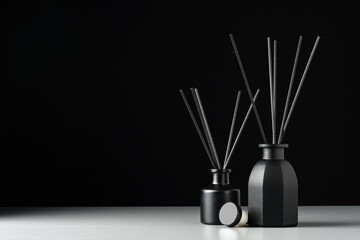 Two Black Reed Diffuser Bottles on White Surface Against Black Background