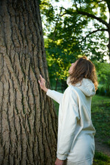 Pretty woman leaning on the old tree. Female hugging huge tree trunk. Girl touches a big tree in a...