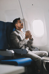 Asian businessman enjoying enjoys a coffee comfortable flight while sitting in the airplane cabin, Passengers near the window.