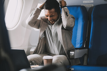 Stressed and professional Asian businessman in a business class, having a serious phone call with someone during the flight to a business meeting.