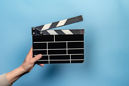 Old clapperboard in a hand, blue background. AI generative