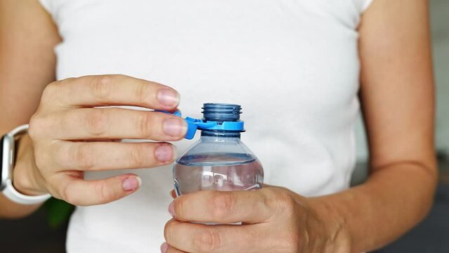 Bottle with stationary plastic cap in woman hand. The new design means the cap remains attached to the bottle after opening, making the entire package easier to collect and recycle