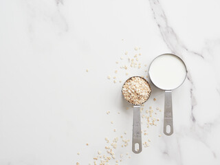 Stainless steel measuring cups with one-half cup of milk and one-quarter cup of oat flakes. Proportion of ingredients to prepare oatmeal porridge.