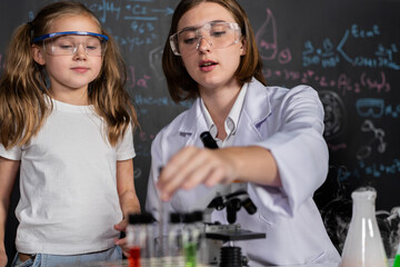 Teacher in support and watch student in laboratory they wear safety glasses, stand and experiment about science of chemistry in STEM class. Student funny do experiment with liquid in tube. Erudition.