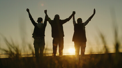 In the evening glow, a family of farmers stands in their field, raising their hands in a triumphant gesture of success. © StockMediaSeller