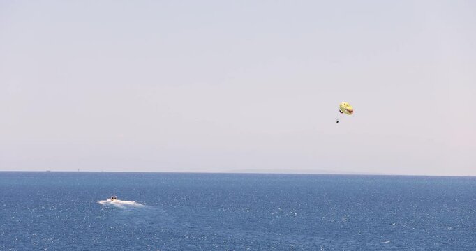 Slow motion footage of a Parasailer who is Parasailing over the ocean in the city of Benidorm in Spain showing the glider being pulled by a speed boat