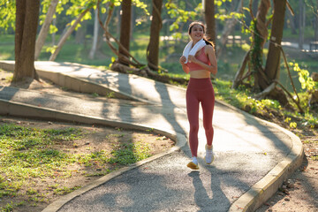 Beautiful Asian female athlete runner doing evening exercise. Happily, female athlete runs under a tree in the park. For good health, keeping your figure, body shape, fitness, healthy food.