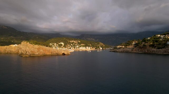 4K Aerial Drone video of popular summer destination, sunset over the cliffs with a lighthouse and a huge port of boats anchored at golden hour with seagulls flying. Port de Soller, Mallorca