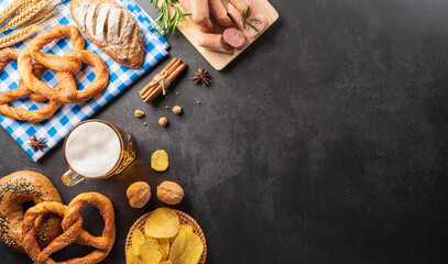 Oktoberfest festival decoration symbols made from Pretzel loaf, beer, and Bavarian white and blue fabric on dark stone background.