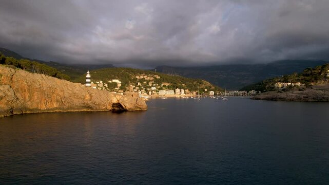 4K Aerial Drone video of popular summer destination, sunset over the cliffs with a lighthouse and a huge port of boats anchored at golden hour with seagulls flying. Port de Soller, Mallorca