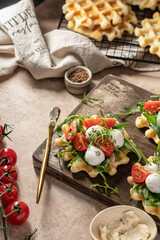 Waffles sandwiches with tomatoes, mozzarella balls, arugula, microgreens on wooden rustic board with ingredients. Homemade breakfast