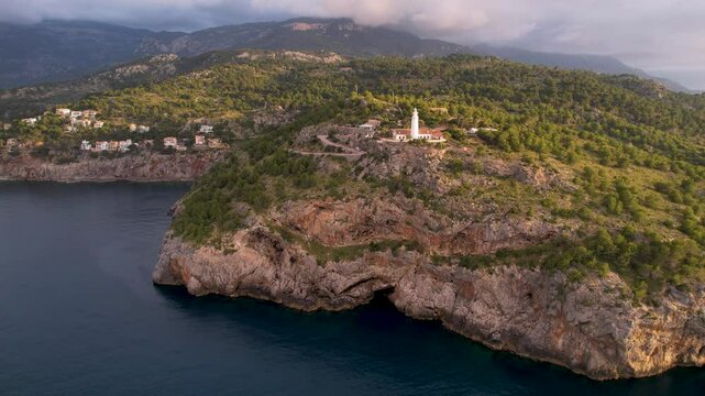 4K Aerial Drone video of popular summer destination, sunset over the cliffs with a lighthouse and a huge port of boats anchored at golden hour with seagulls flying. Port de Soller, Mallorca