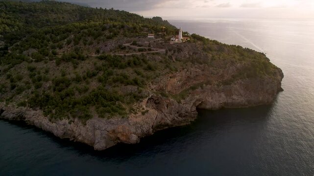 4K Aerial Drone video of popular summer destination, sunset over the cliffs with a lighthouse and a huge port of boats anchored at golden hour with seagulls flying. Port de Soller, Mallorca