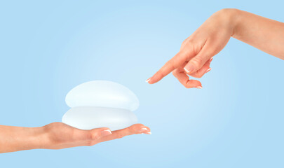 Female hand pointing on breast implants on blue background. Plastic surgery, copy space