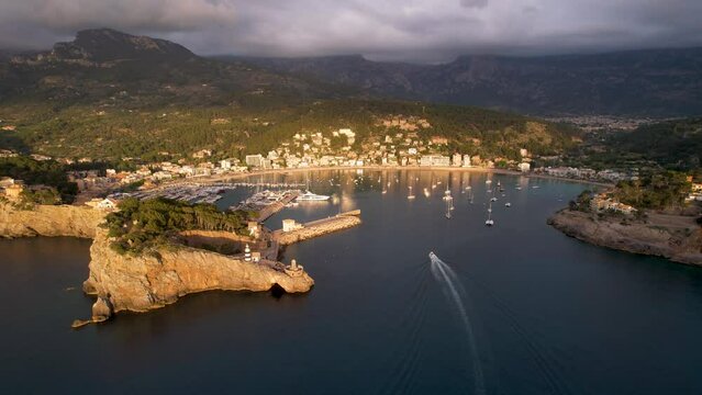 4K Aerial Drone video of popular summer destination, sunset over the cliffs with a lighthouse and a huge port of boats anchored at golden hour with seagulls flying. Port de Soller, Mallorca