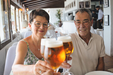 Retired couple celebrating their son's successes in a restaurant. Family toasting with glasses of beer.