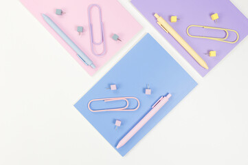 Top view of pink, purple and blue notebooks on white background. Colorful pens, paperclips, pins, school, office wallpaper. Flat lay, copy space.