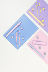 Top view of pink, purple and blue notebooks on white background. Colorful pens, paperclips, pins, school, office wallpaper. Flat lay, copy space.