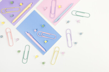 Top view of pink, purple and blue notebooks on white background. Colorful pens, paperclips, pins, school, office wallpaper. Flat lay, copy space.