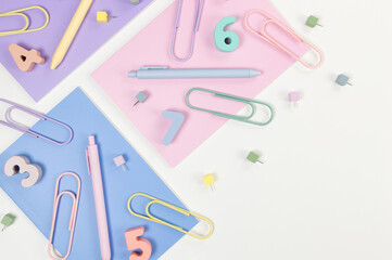 Top view of pink, purple and blue notebooks on white background. Colorful pens, paperclips, numbers and pins. School, office wallpaper. Flat lay, copy space.