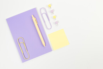 Top view of purple notebook on white background. Sticky note, paperclips, pen and pins. School, office wallpaper. Flat lay, copy space.