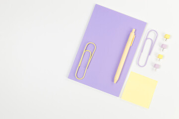 Top view of purple notebook on white background. Sticky note, paperclips, pen and pins. School, office wallpaper. Flat lay, copy space.