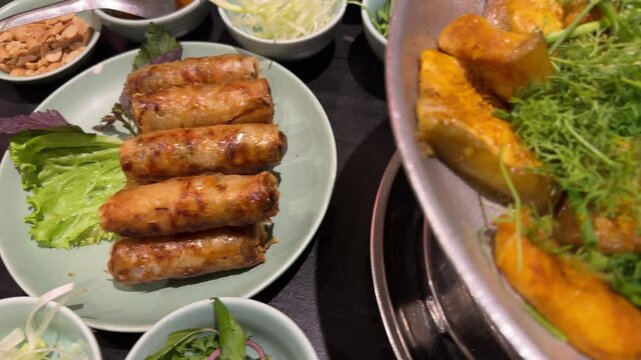 Vietnamese fried spring rolls Nem Ran on table near of traditional dish fried river catfish with cilantro and spring onion,  popular dish of boneless grilled hemibagrus fish in Vietnam.