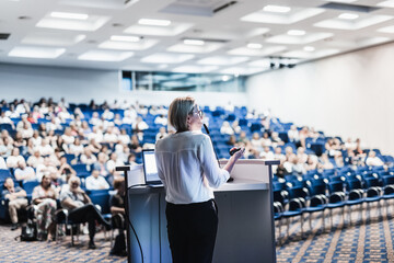 Obraz premium Female speaker giving a talk on corporate business conference. Unrecognizable people in audience at conference hall. Business and Entrepreneurship event