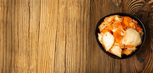 Kimchee in black bowl on wood table. Spicy kim chi pile, hot fermented napa cabbage, traditional jimchi