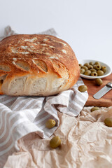 Freshly baked rustic artisan bread with green olives, presented on a striped cloth and wooden board