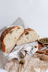 Freshly baked rustic artisan bread with green olives, presented on a striped cloth and wooden board
