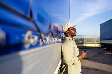Driver standing by his truck and using mobile phone.