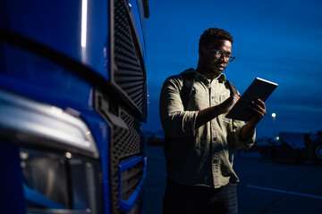 Professional truck driver holding digital tablet preparing for the night drive.