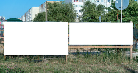 Blank white billboards in front of residential buildings. Empty advertisement space in urban setting with green grass