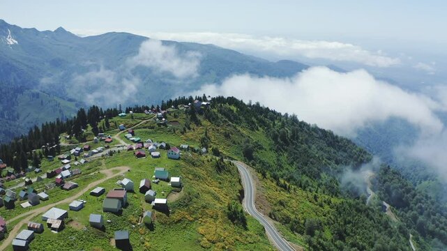 Aerial drone shot of Gomismta, village within Guria region of Georgia, surrounded by lush greenery and alpine mountains, with picturesque layout of homes and winding village roads visible above cloud