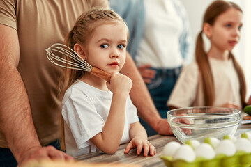In a heartwarming family moment, a little girl joyfully uses a whisk in the kitchen