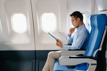 Fototapeta premium Asian male passenger of airplane sitting in comfortable seat while working laptop and tablet with mock up area using wireless connection. Travel in style,
