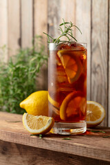 Iced tea or alcoholic cocktail with ice, rosemary and lemon slices on a old wooden table.