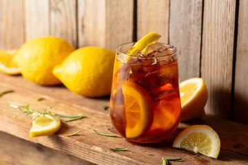 Iced tea or alcoholic cocktail with ice, rosemary and lemon slices on a old wooden table.