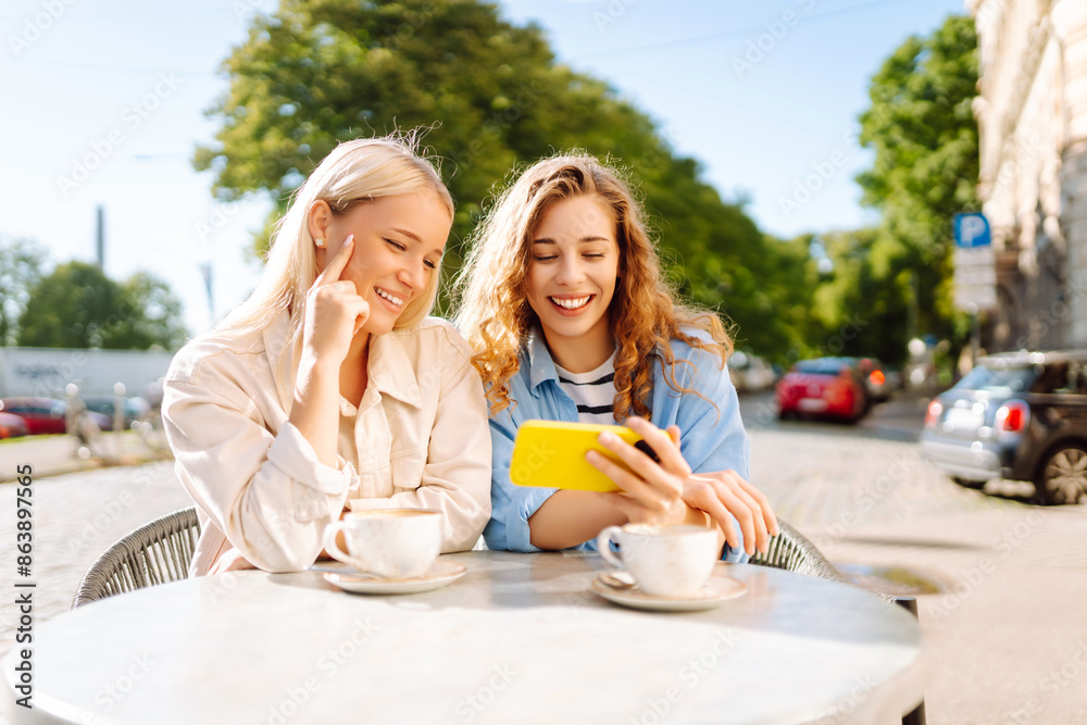 Wall mural two young women, sisters, best friends showing news social media photos on smart phone cellphone sit