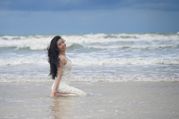 Fototapeta premium Happy woman in a white dress sitting and playing on the beach