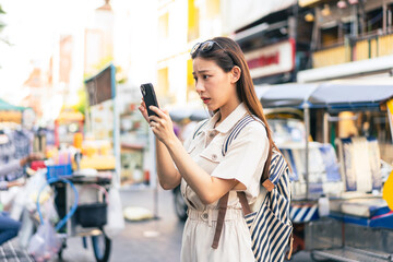 Young Asian woman getting lost and using map on a mobile phone while traveling and backpacker in Khaosan Road outdoor market in Bangkok, Thailand