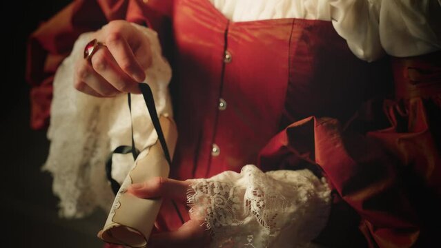 fantasy woman queen close-up hands holds receives opens letter antique style papyrus scroll tied with ribbon Body part face cropped. girl reads love text. old style Vintage dress white red gown art 