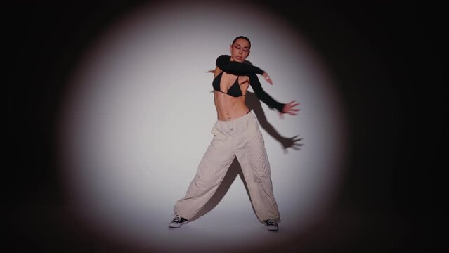Handsome female dancer performing modern dance in white light spot with red color flashing lights in studio environment. Sexy woman demonstrates contemporary choreography aggressive moves, handheld