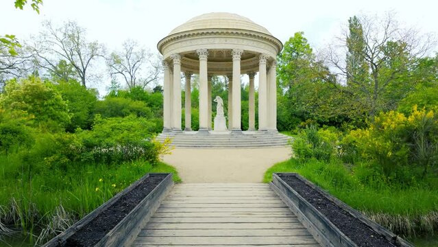 A gazebo with columns and a stone statue surrounded by trees and bushes