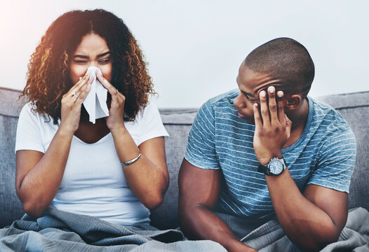 Frustrated couple, sick and argument with fight on sofa in disagreement, conflict or allergies at home. Man or woman blowing nose with tissue for flu, cold or illness in breakup or toxic relationship