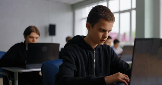 Students In Computer Classroom In School, Portrait Of Concentrated Teen Boy With Laptop