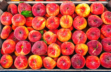 A top view of fresh Saturn peaches arranged in a wooden crate at a market.